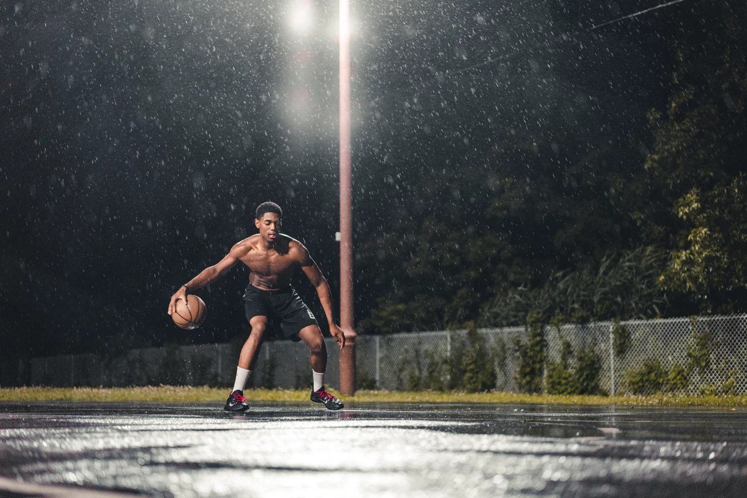 A man playing basketball in the rain.