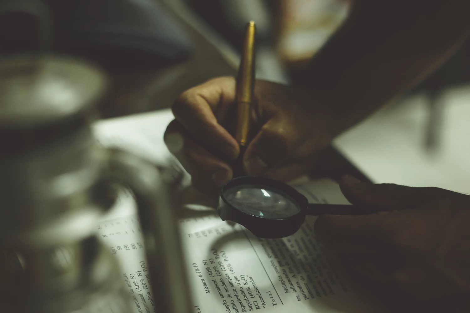 A person writing in a book while holding a magnifying glass.